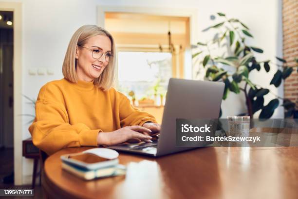 Portrait Of Middle Aged Woman Sitting At Dinning With Laptop Working At Home Stock Photo - Download Image Now