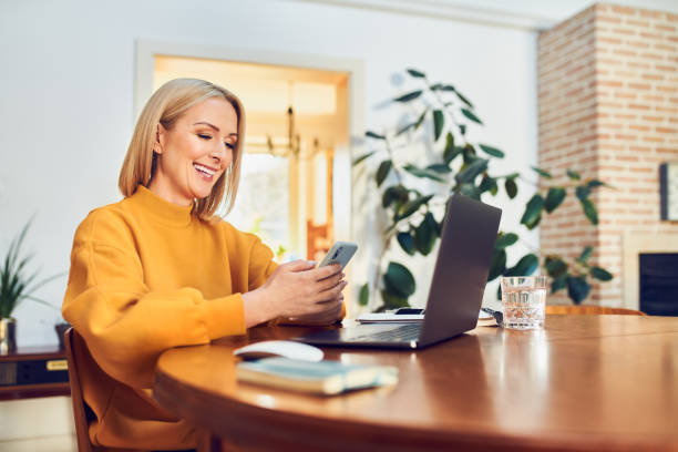 istock Laughing mid adult woman using smart phone while working remotely at home 1395474822