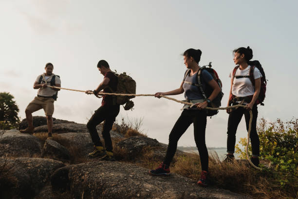 um grupo de turistas homens e mulheres escalando quatro mochileiros asiáticos puxando cordas para escalar a montanha. - 2802 - fotografias e filmes do acervo