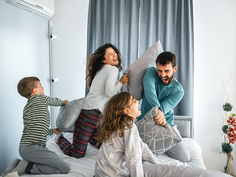 Happy family wearing sleepwear sitting on bed fighting with pillows