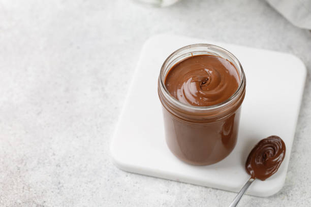 숟가락으로 항아리에 액체 초콜릿을 말리십시오. 화이트 보드에 초콜릿 소스, 타일 배경 - unhealthy eating flash 뉴스 사진 이미지