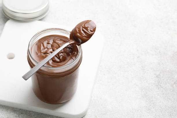 istock Spoon with Chocolate sauce on glass jar and white board. Liquid chocolate. Copy space 1395486910