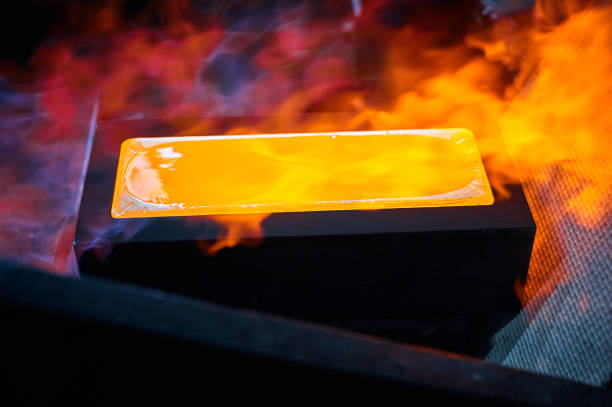 Hot gold ingot chills in graphite casting form on workbench in shielding gases at jewelry production plant extreme close view