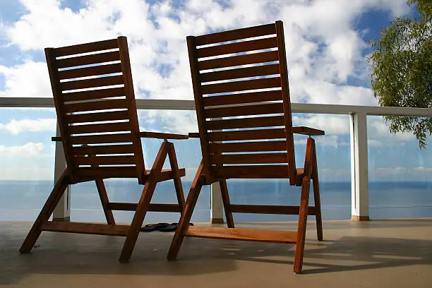 Two matching wood chairs on deck overlooking ocean.