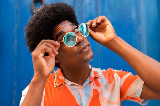 Confident young black man with afro hairstyle putting on sunglasses outdoors. Lifestyle concept.