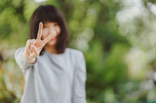 Woman happy smile with v sign hand gesture with nature background, Victory and peace sign concept. Selective focus.
