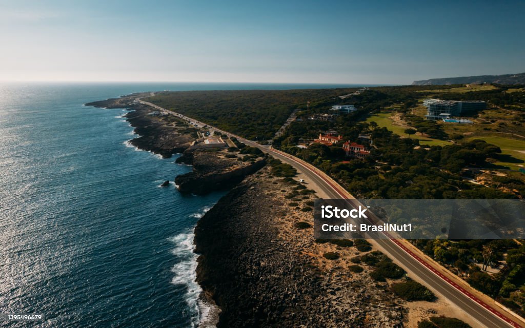 Aerial view top down view of of a straight road and rugged coastline at Guincho beach, Cascais, Portugal Aerial view top down view of of a straight road and rugged coastline at Guincho beach, Cascais, Portugal. Cabo da Roca is visible at the far right corner Beach Stock Photo