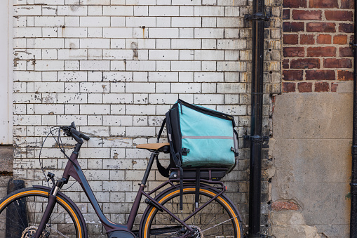 An electric bike leaning against a brick wall in Newcastle Upon Tyne, England with a delivery bag placed on the carrier at the rear of the bike.