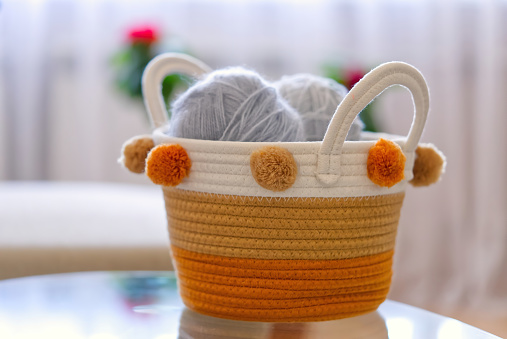 Top view of a wicker basket with balls of wool yarn for hand knitting and a set of hooks and knitting needles on an old wooden table. close up