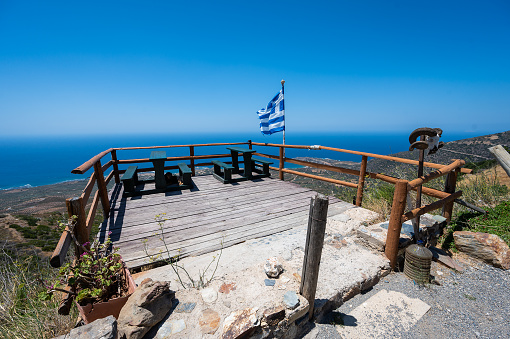Amazing Terrace, Greek Flag with view over Island Crete, Greece. Wooden terrace in a restaurant or bar looking at the sea and beaches of western Crete with Greek flag waving in the wind.