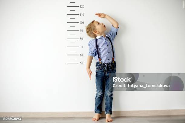 Little Child Boy Measuring Height Against Wall In Room Stock Photo - Download Image Now