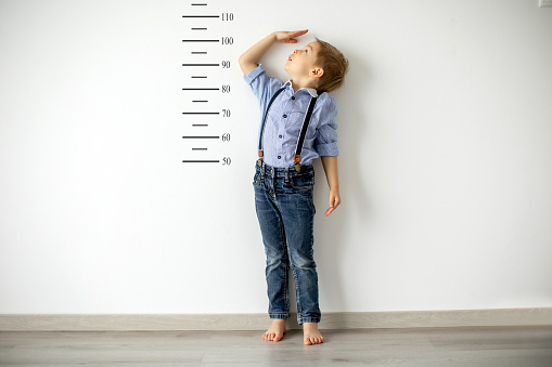 Little child, blond boy, measuring height against wall in room