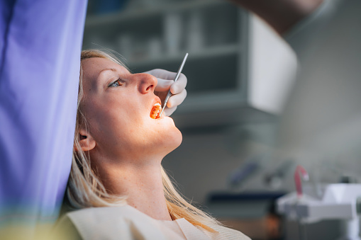 Close-up of young female with open mouth at the dentist office while doctor examining her oral cavity