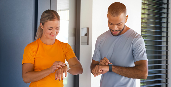 Smiling young man and woman checking time on smart watch while standing together.