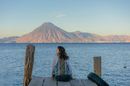 Young Caucasian woman  sitting on pier on Atitlan Lake in Guatemala at sunset