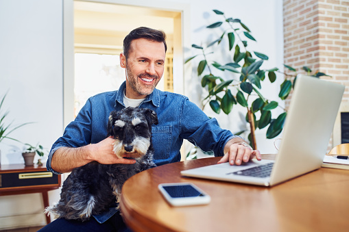 Man holding dog on lap while using laptop at home