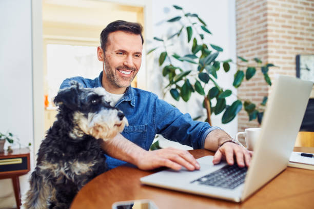 istock Happy man using laptop working from home with dog sitting on lap 1395512256