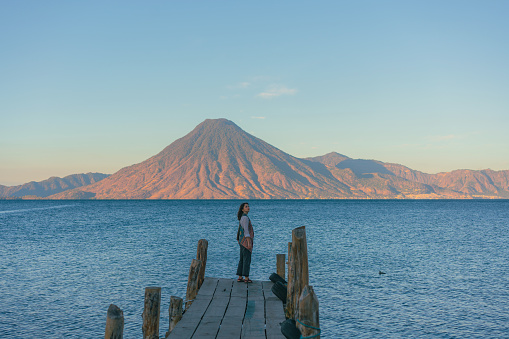 Young Caucasian woman  standing on pier on Atitlan Lake in Guatemala at sunset