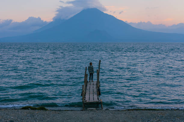 istock Man standing on pier on Atitlan Lake in Guatemala at sunset 1395513546