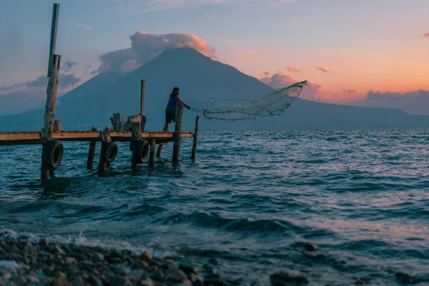Aerial of a small fisherman village of Panajachel on Lake Atitlan in Guatemala during sunrise, displaying the lake and the boats in the foreground with the houses and streets in the background