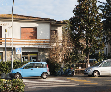 Ghezzano, Italy - December 22, 2021: a car and a motor scooter are parked on the pedestrian crossing just in front of a local Post Office. Ghezzano is a small town belonging to San Giuliano Terme in the province of Pisa. Such behaviours are totally common and usually not sanctioned.