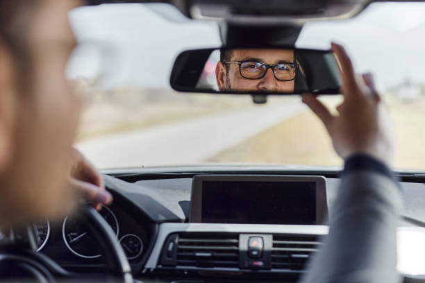 Reflection of a man adjusting rear-view mirror in a car.