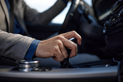 Close up of unrecognizable businessman holding his hand on automatic gearshift while driving a car.