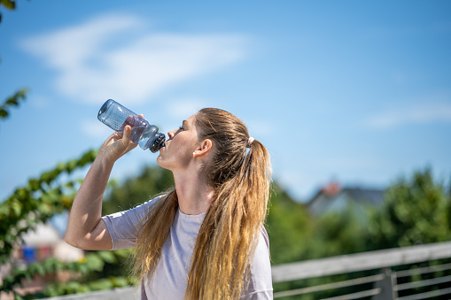Young woman drinking water after jogging in public park.