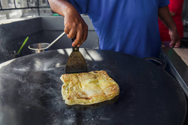 Unrecognizable Chef Cooking Roti Canai Close-up shot of unrecognizable man cooking roti canai above a hot plate flat pan at street foods bazaar. roti canai stock pictures, royalty-free photos & images