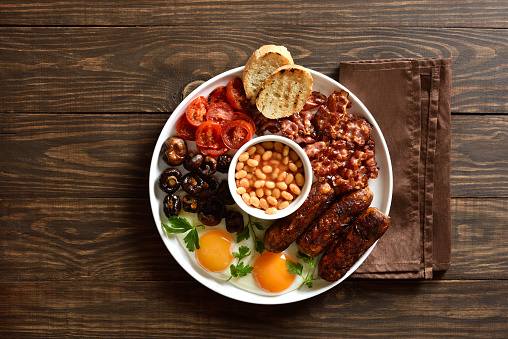 Full English breakfast with fried egg, bacon, sausage, beans and mushrooms on wooden background. Top view, flat lay