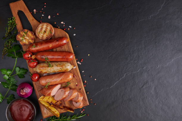 saucisses et ingrédients pour la cuisson. saucisse grillée avec ajout d’herbes et d’épices, légumes, romarin, thym sur l’assiette de gril, grillades, barbecue, barbecue, sur table en pierre. vue de dessus. - barbecue grill chef barbecue sausage photos et images de collection