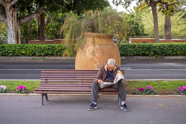Man sitting on a park bench and reading a newspaper in the center of Santa Cruz which is the main city on the Spanish Canary Island Tenerife