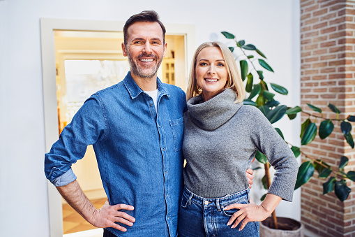 Cheerful middle aged couple homeowners standing together at home