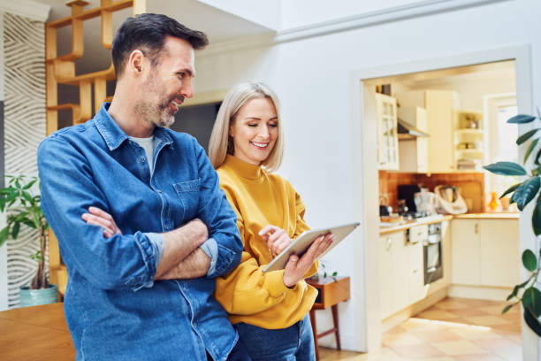 istock Happy middle aged couple standing at home with digital tablet talking 1395525172
