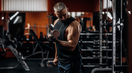 Handsome sportsman bodybuilder weightlifter pumping biceps in gym