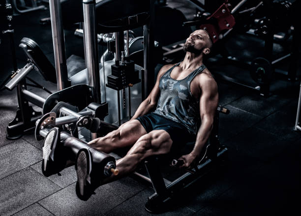 istock Muscular athlete using weights machine for legs at the gym. Hard training in gym 1395530180