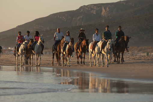 Zahara de los Atunes, Spain - Sept 09, 2021: A group of people, tourists, enjoy an organized horseback ride, along the seashore, on the beach, on a summer afternoon