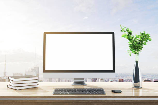 Close up of modern designer desktop with books, empty white computer screen, decorative plant, supplies and bright city and sky view background. Mock up, 3D Rendering. stock photo