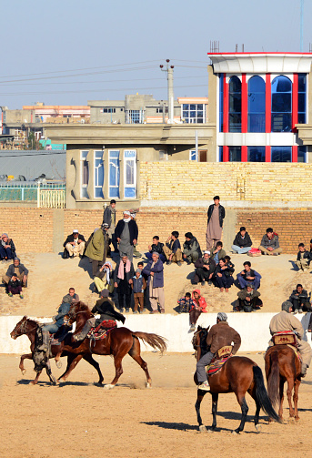 Mazar-e-Sharif, Balkh province, Afghanistan: rider with the calf  and spectators at a match of Buzkashi aka Afghan polo, Afghanistan's national sport - horse-mounted players fight for a calf carcass - admission is open and free.