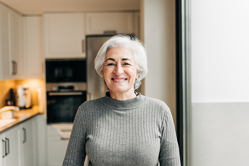 Carefree senior woman smiling at the camera while standing in her home. Happy grey-haired woman enjoying her retirement years at home.