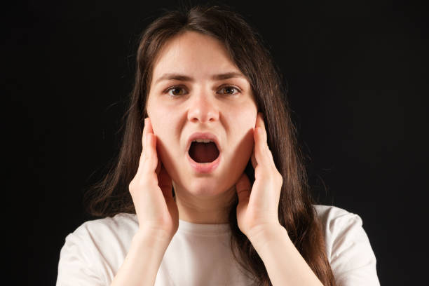 口が開いている女性は、両手で頬を握り、顎関節の機能不全のために運動します - ヒトのアゴの骨 ストックフォトと画像