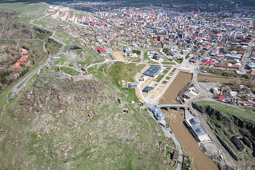 Ancient stone bridge across Kars River & Kars Castle - main tourist attractions of Kars, Turkey. Near flag (on castle) are portrait of Ataturk & writing in Turkish 'Motherland remembers you'