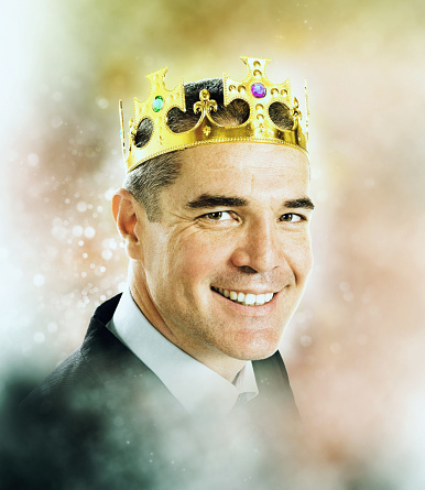 Confident, handsome man wearing a crown looks at the camera, smiling happily.