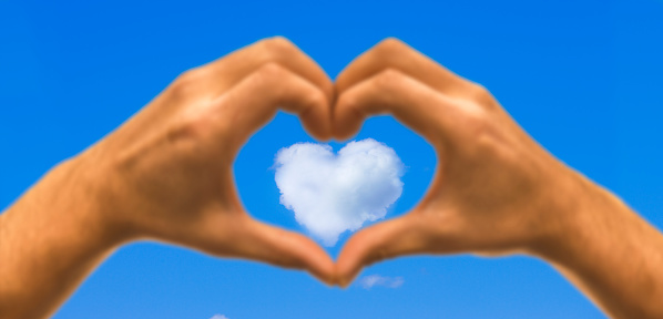 Hand heart in front of a blue sky with cloud heart