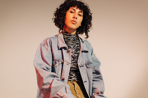 Stylish young woman looking at the camera while wearing a denim jacket and jewellery. Fashionable young woman feeling confident in her style.