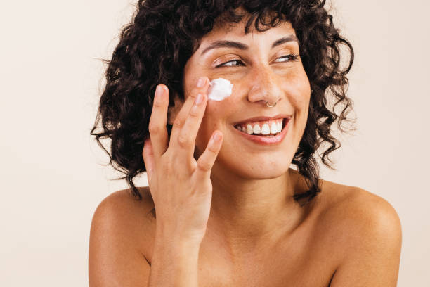 istock Happy young woman applying moisturizing cream on her face 1395541240