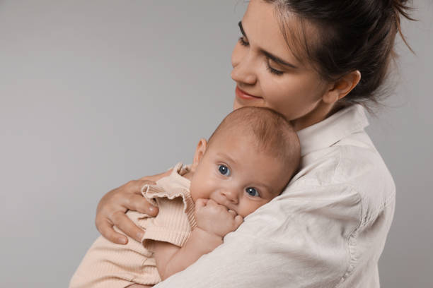 istock Beautiful mother with her cute baby on grey background. Space for text 1395542135
