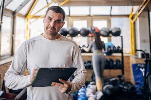 Portrait of young fit male fitness instructor holding a clipboard in gym.