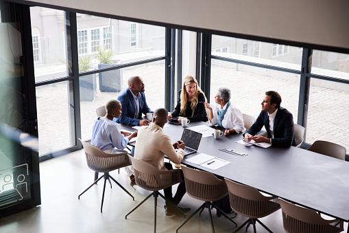 Group of diverse businesspeople talking together around a conference table during a boardroom meeting in a modern office