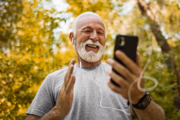 istock Senior man in autumn park using smartphone making video call 1395547524